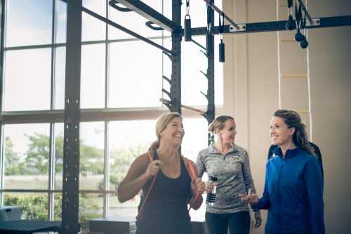 A gym scene featuring three women conversing, highlighting friendship and support in a fitness environment.