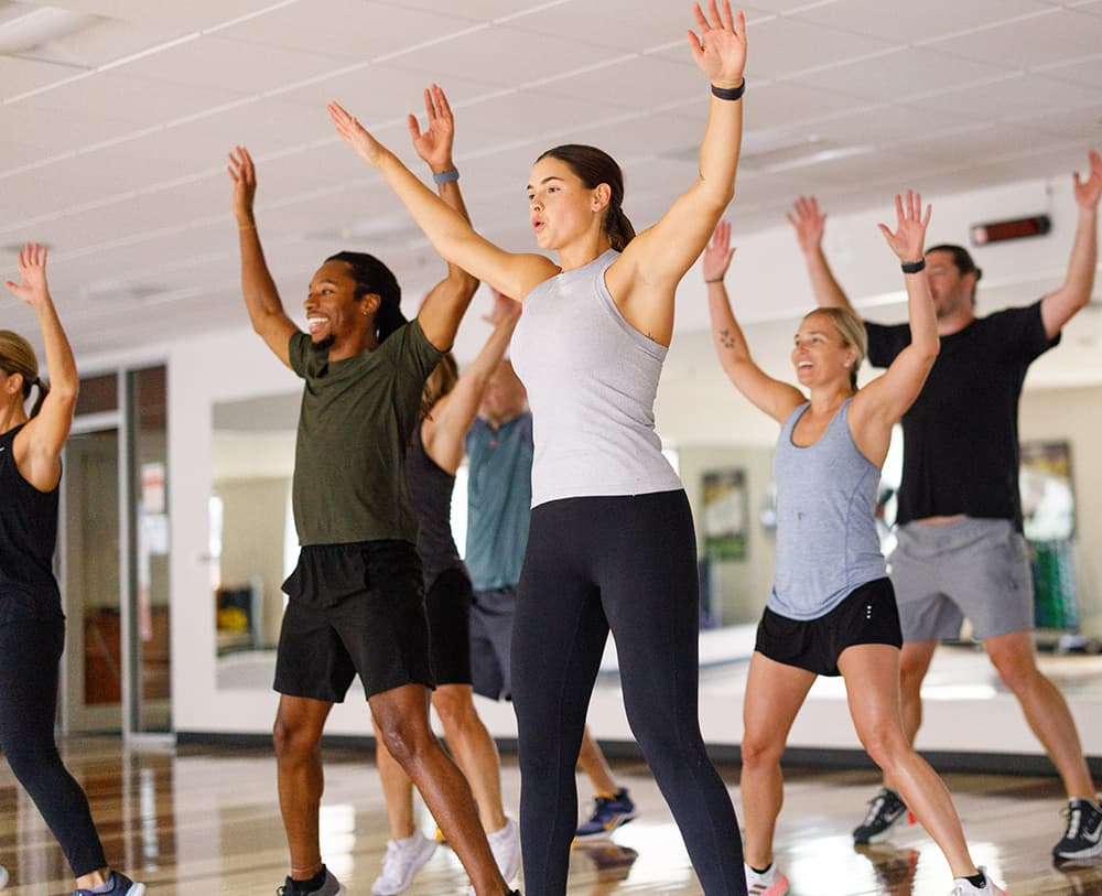 People do jumping jacks in cardio group fitness class