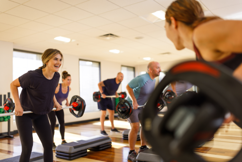 A diverse group of individuals exercising in a gym, lifting weights and engaging in fitness activities together.